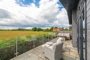 Eine Terrasse mit Gartenmöbeln, Blick auf ein Feld und ein Haus im Hintergrund.