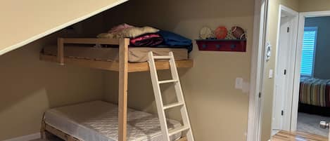 Una cama litera con escalera, un estante decorado con motivos deportivos y una puerta que da a otra habitación.