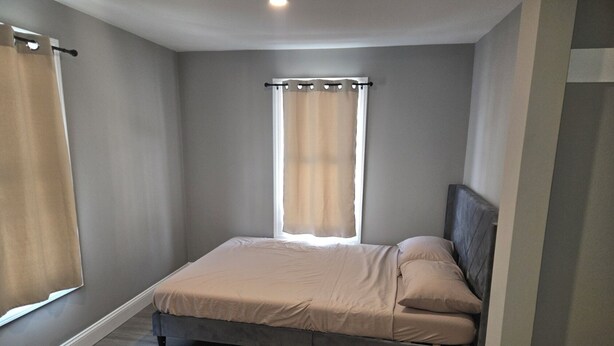 A bedroom with a bed, a window with curtains, and a wooden floor.