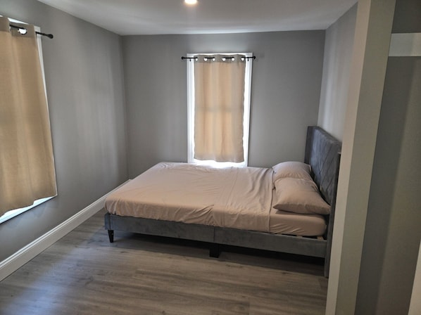 A bedroom with a bed, a window with curtains, and a wooden floor.