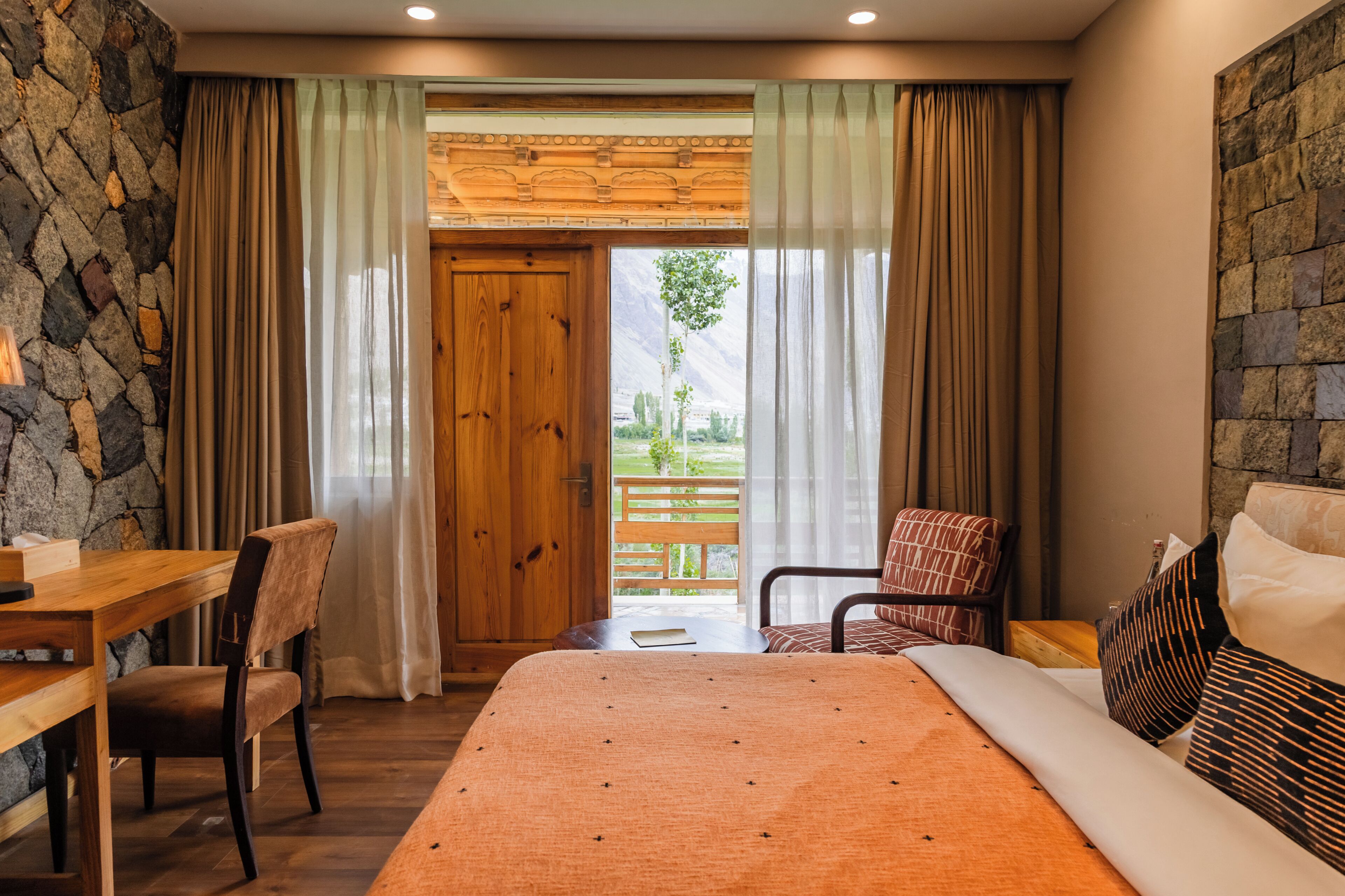 A bedroom with a wooden door, a bed, a desk, and a chair.