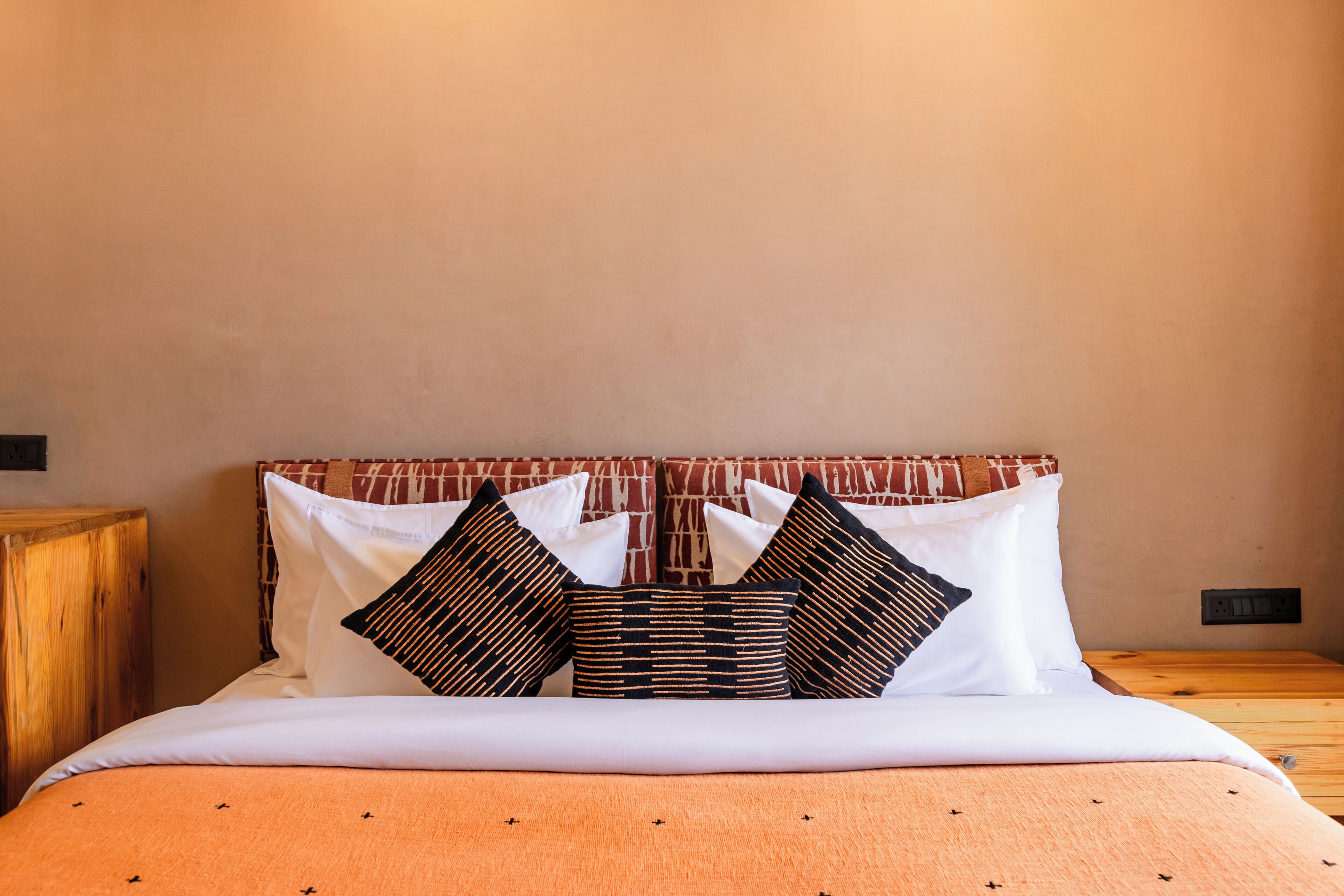 Una cama con un cabecero estampado, almohadas blancas y una colcha naranja.