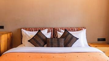 Una cama con un cabecero estampado, almohadas blancas y una colcha naranja.
