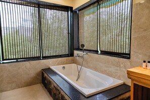 A bathroom with a bathtub, a shower, and a window with a view of greenery. - Aksai Boutique Hotel (Diskit)