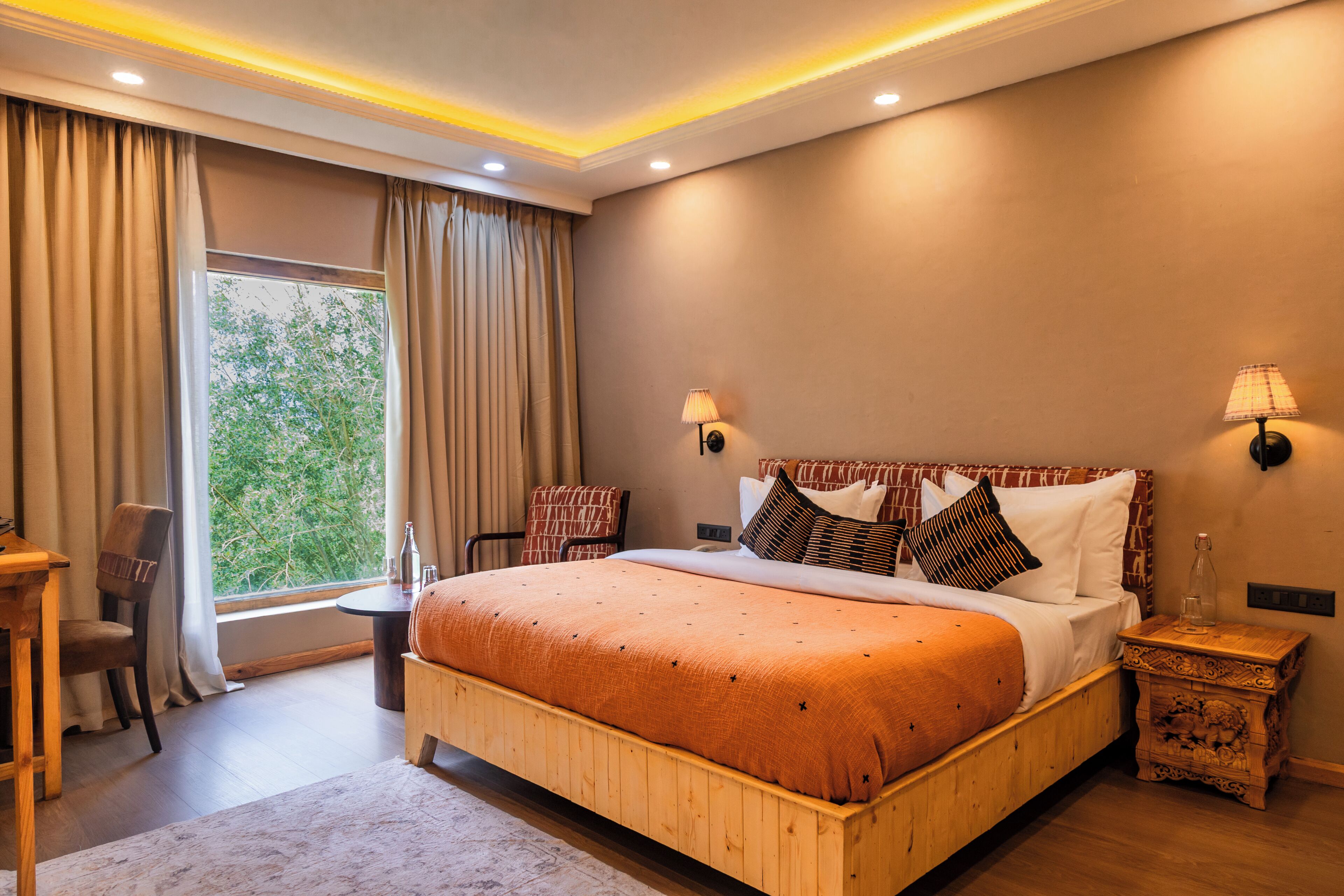 Quarto com uma cama grande, mesa de cabeceira de madeira, escrivaninha e uma cadeira.