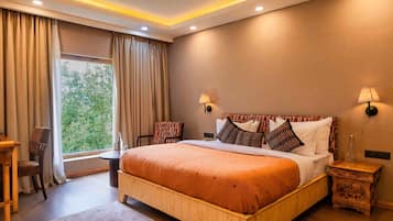 A bedroom with a wooden bed, a desk, a chair, and a view of greenery through the window.