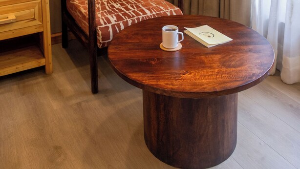 Una stanza con un tavolo rotondo in legno, una poltrona a motivi decorativi, un piccolo tavolino in legno e una bottiglia.