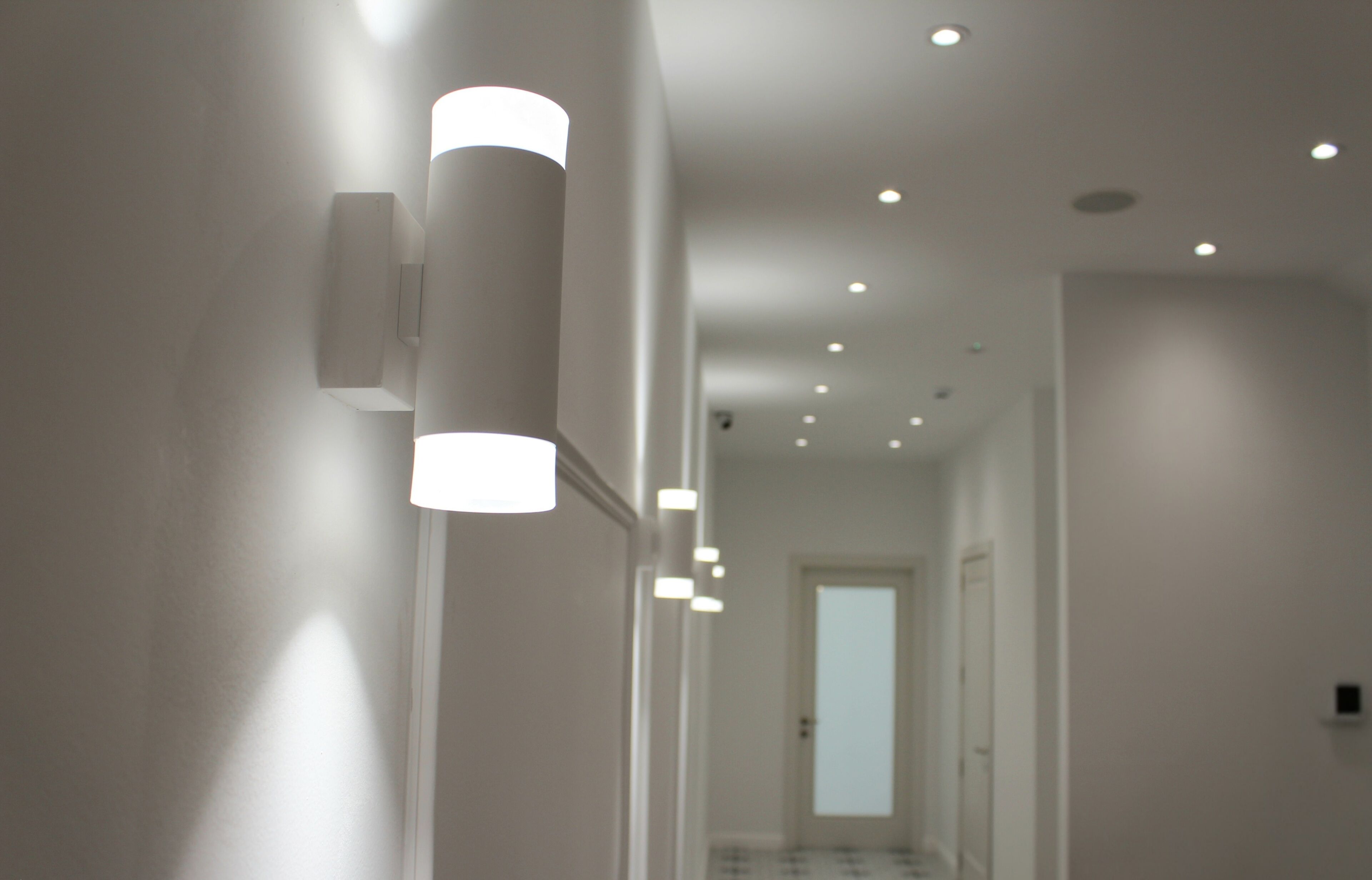 Un couloir avec des spots encastrés au plafond et une porte au fond.