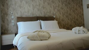 A neatly made bed with white linens and a folded towel, a wooden headboard, and a patterned wallpaper.