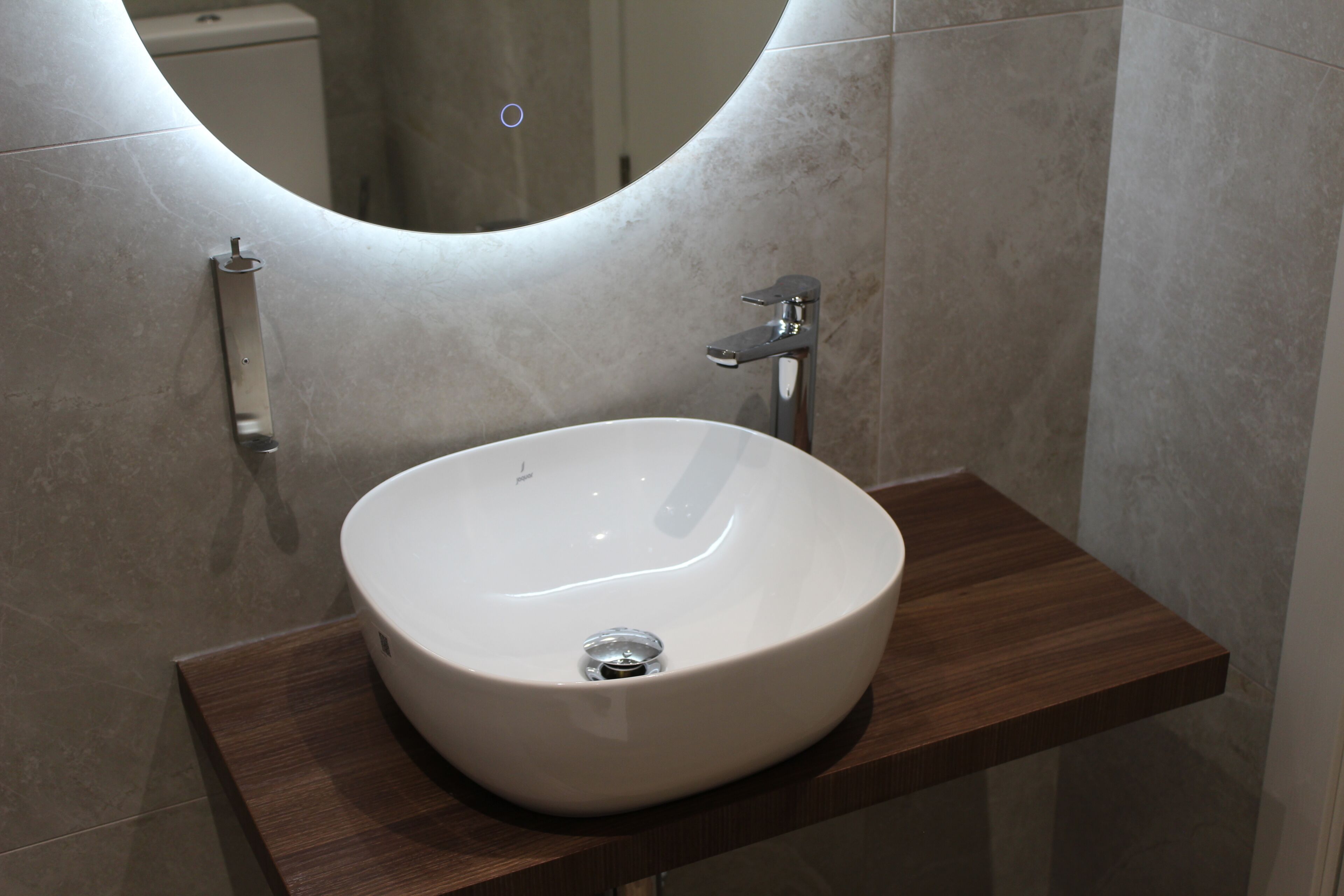 A bathroom with a white sink, a mirror, and a wooden shelf.