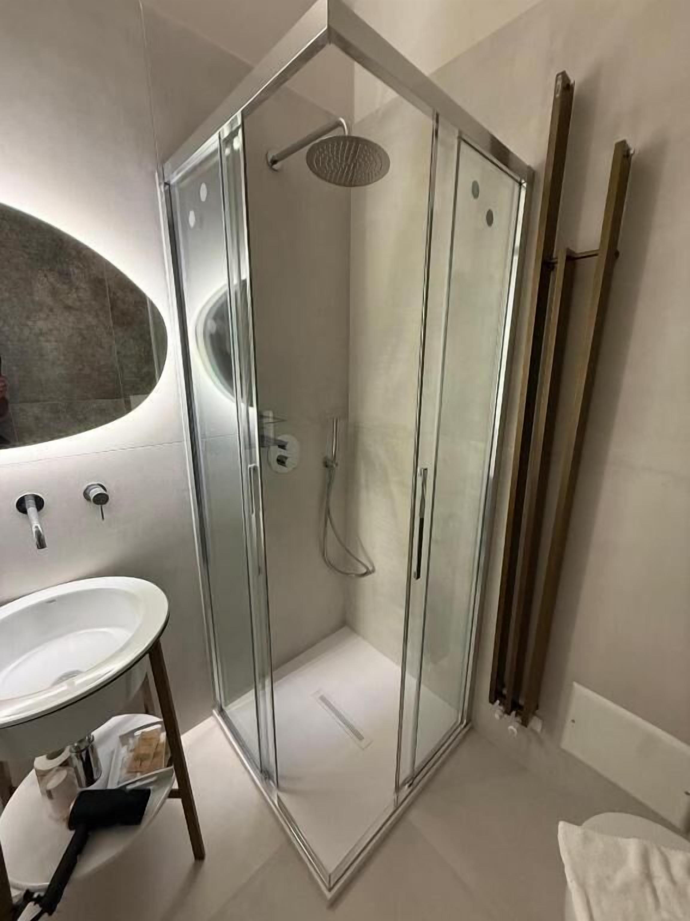 Un baño moderno con ducha de vidrio, un lavamanos blanco y un espejo grande.