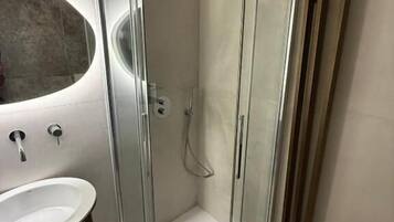 Un baño moderno con ducha de vidrio, un lavamanos blanco y un espejo grande.