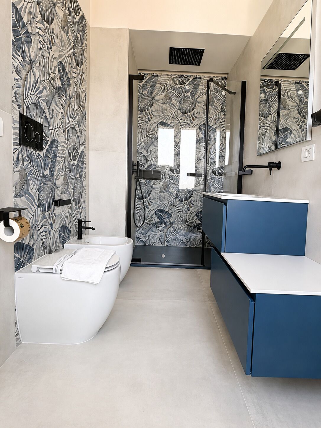 Un baño moderno con una bañera blanca, un tocador azul y una zona de ducha con puerta de cristal.