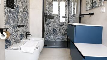 Un baño moderno con una bañera blanca, un tocador azul y una zona de ducha con puerta de cristal.