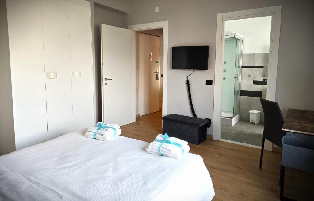A hotel room with a bed, a desk, a television, and a shower area.