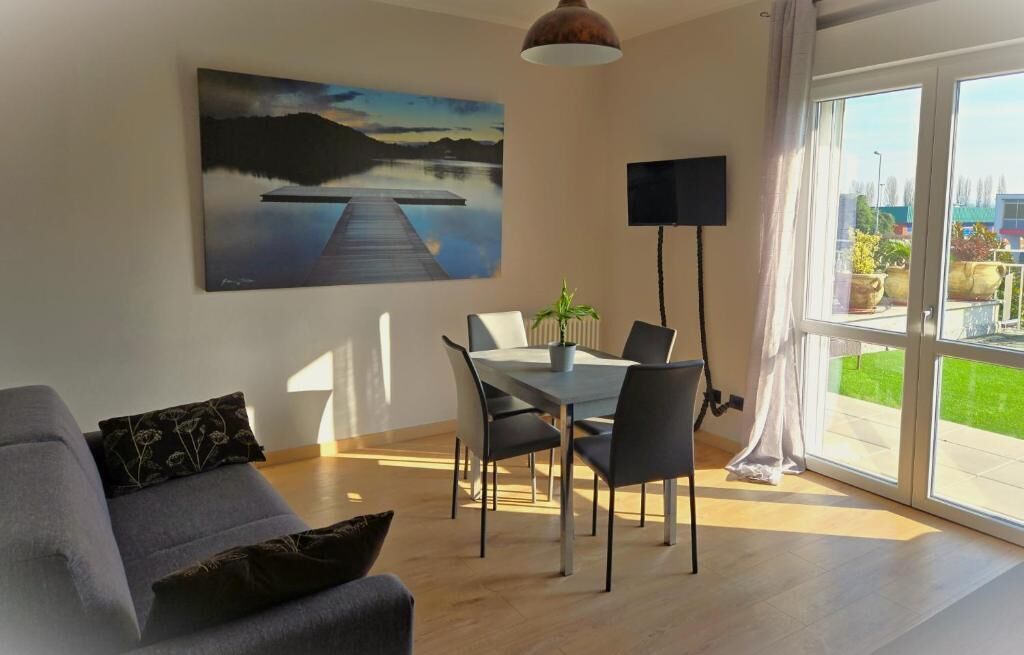 Ein modernes Wohnzimmer mit Essbereich, einem großen Fenster mit Vorhängen, einem Flachbildfernseher und einem Gemälde einer Landschaft mit See.