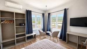 Habitación de hotel con cama, escritorio, silla, televisión, armario y ventana con cortinas.