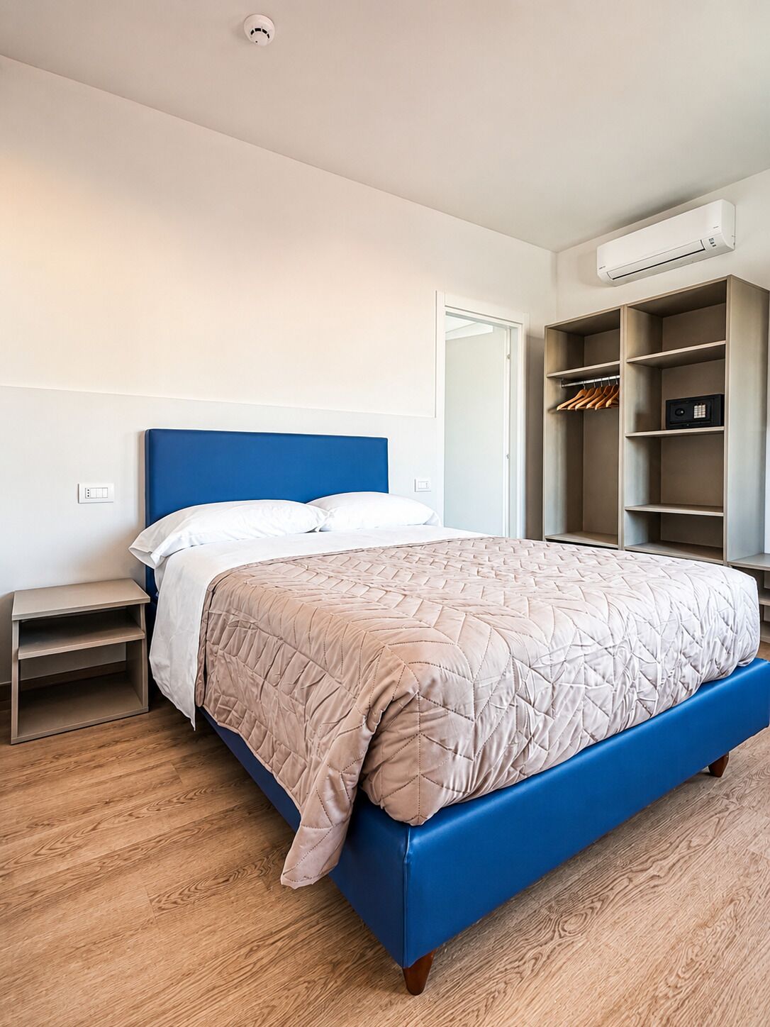 Un dormitorio con cama, mesitas de noche, armario y aire acondicionado.
