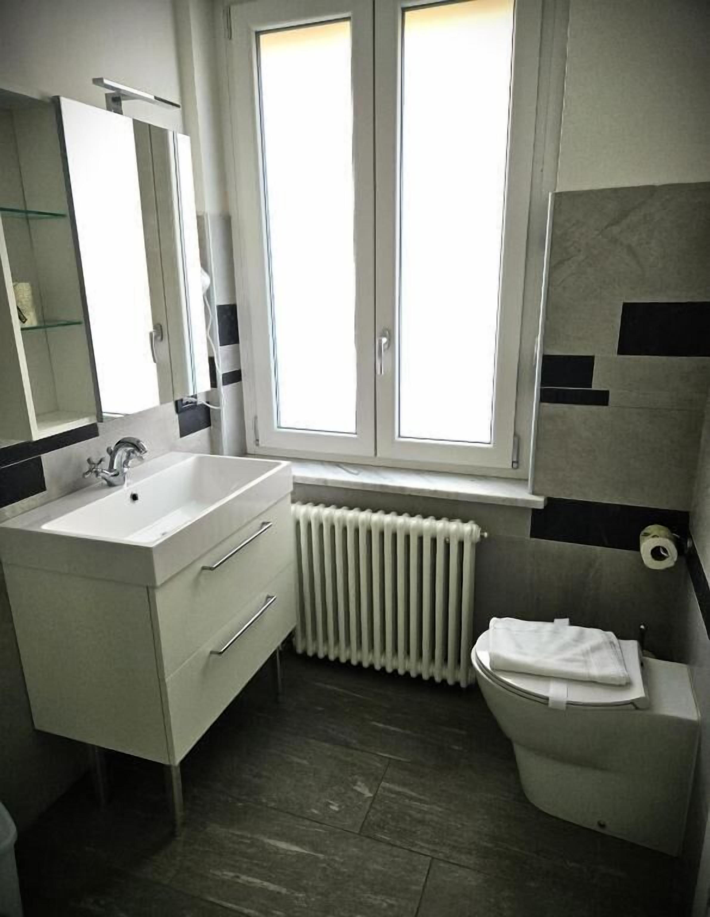 Un baño con lavamanos blanco, un espejo, una ventana y un inodoro.