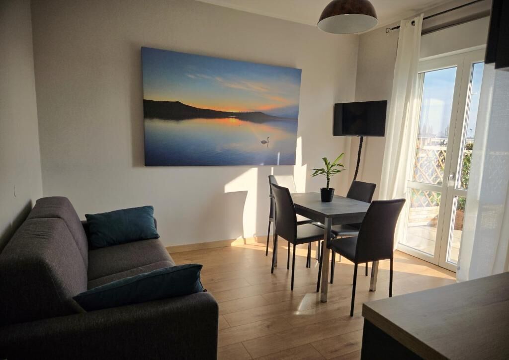 Ett vardagsrum med en soffa, ett matbord med stolar, en platt-TV och en tavla som föreställer en solnedgång över vattnet.