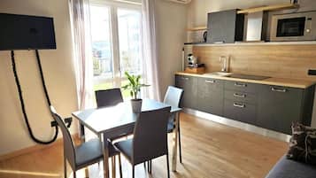 Una cocina moderna con microondas, horno y armarios de madera. Hay una mesa de comedor con sillas y una planta en maceta.