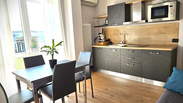 A modern kitchen with a microwave, cabinets, and a dining area with chairs and a table. - Seven Lakes ApartHotel RTA (Burolo)