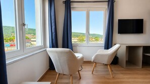 Una habitación con dos sillas, un televisor y un ventanal con cortinas.