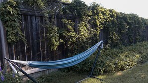 Un hamac est installé contre une clôture en bois, entouré de verdure.