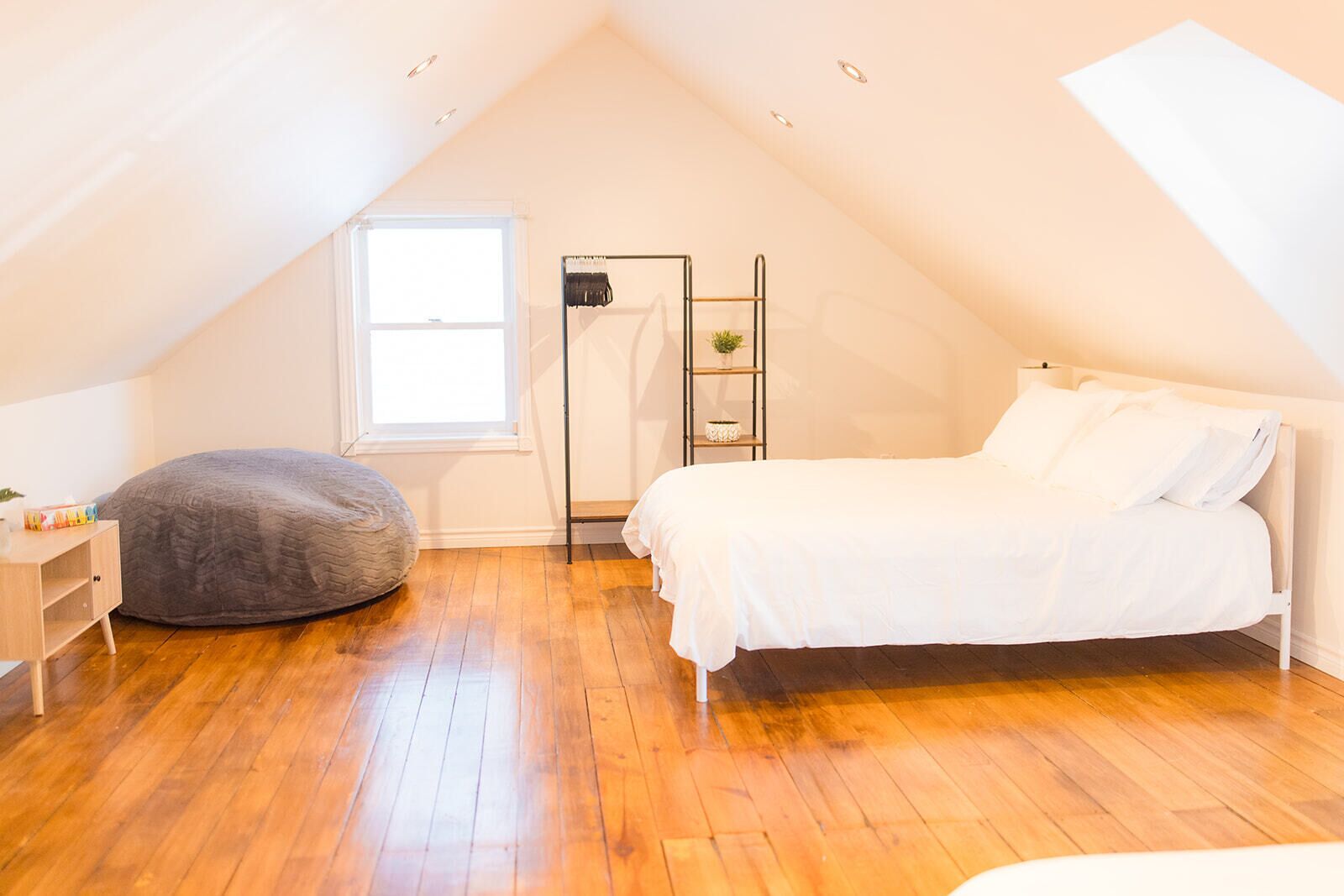 Un dormitorio con cama tipo litera, un sillón de plumas, una mesita y una ventana.