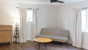 Une pièce comprenant un canapé, une petite table ronde, une commode et un lampadaire.