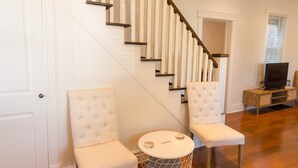 Un escalier aux murs blancs et aux marches en bois, deux fauteuils rembourrés, une petite table ronde et un téléviseur posé sur un meuble en bois.