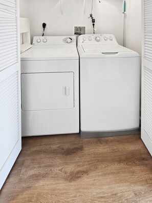 A laundry room with two white front-loading washing machines and dryers, a wooden floor, and a white wall with a power outlet and a light switch. - 2 Bedroom 2 Bathroom Condo With Outdoor Pool! Summer House 303 (Ocean City)