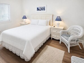 A bedroom with a large bed, two bedside tables with lamps, a wicker chair, and a framed picture on the wall. - 2 Bedroom 2 Bathroom Condo With Outdoor Pool! Summer House 303 (Ocean City)