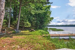 A lakeside cabin with a dock, surrounded by dense trees and a clear sky.