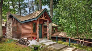En rustik hytte med trævægge, en stenvægskamin, en veranda og en trappe til indgangen.