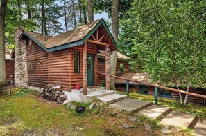 A rustic log cabin with a stone chimney, a porch, and a staircase leading to the entrance. - Stepaway Vacation Rentals- Stoney End (St.Germain)