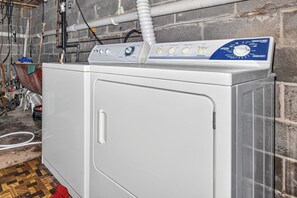 A front-loading washing machine with a control panel, located in a laundry room with a brick wall and various pipes. - Stepaway Vacation Rentals- Stoney End (St.Germain)