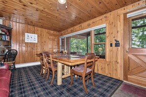 A wooden cabin interior with a dining table, chairs, a red couch, and a large window. - Stepaway Vacation Rentals- Stoney End (St.Germain)