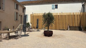An outdoor patio area with a table and chairs, a potted tree, and a wooden fence. - Pèira House • Swimming pool in the heart of the estate (shared with only one other house) (Bages)