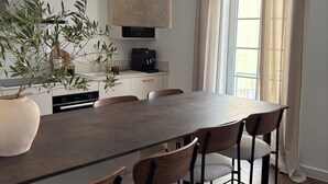 A modern dining area with a large table, six chairs, a hanging light fixture, a coffee machine, and a potted plant. - Pèira House • Swimming pool in the heart of the estate (shared with only one other house) (Bages)
