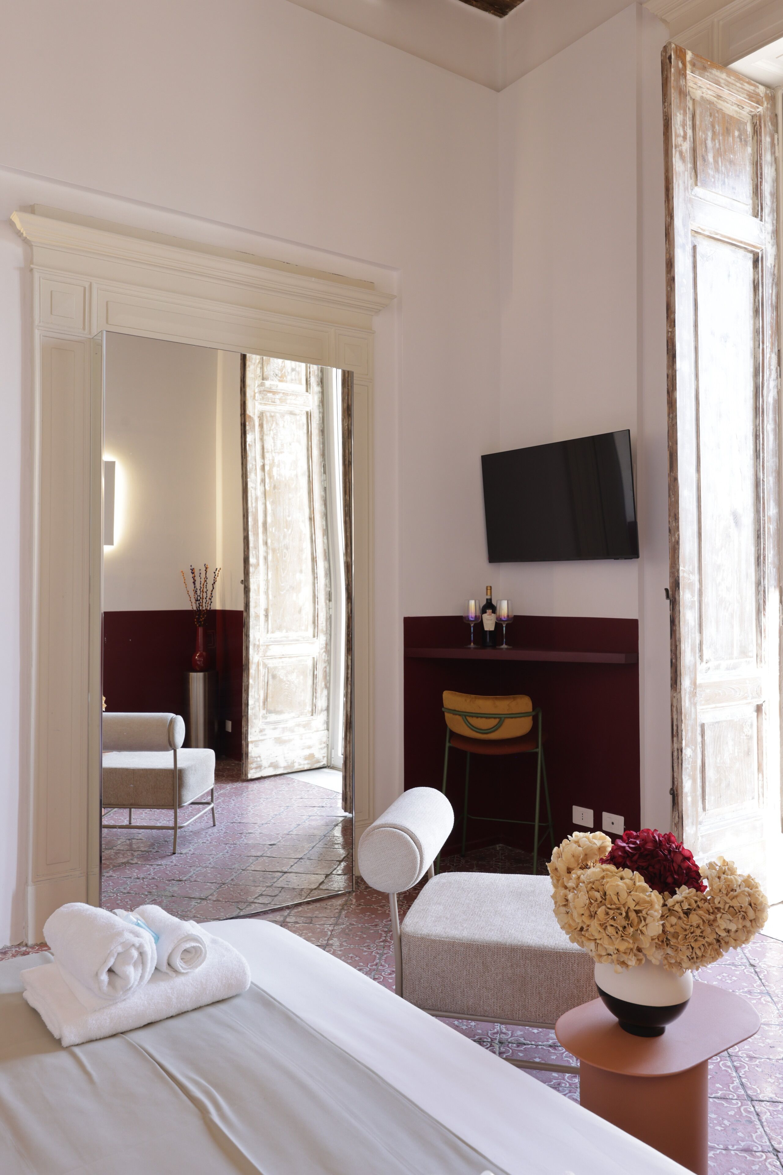 Una habitación de hotel con cama, escritorio y silla, televisor y un florero con flores.
