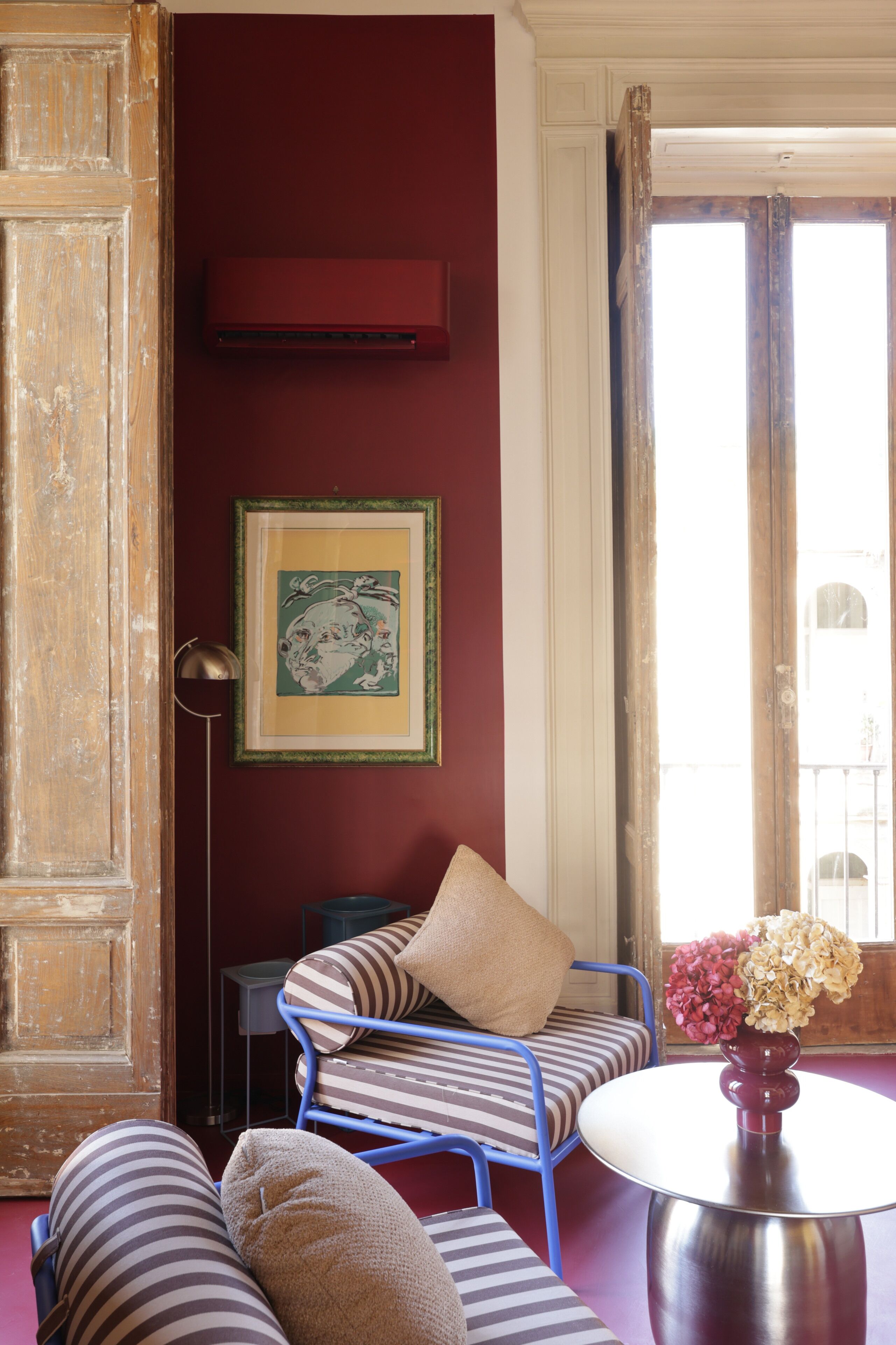 A room with a blue chair, a striped sofa, a framed picture, and a table with a vase.