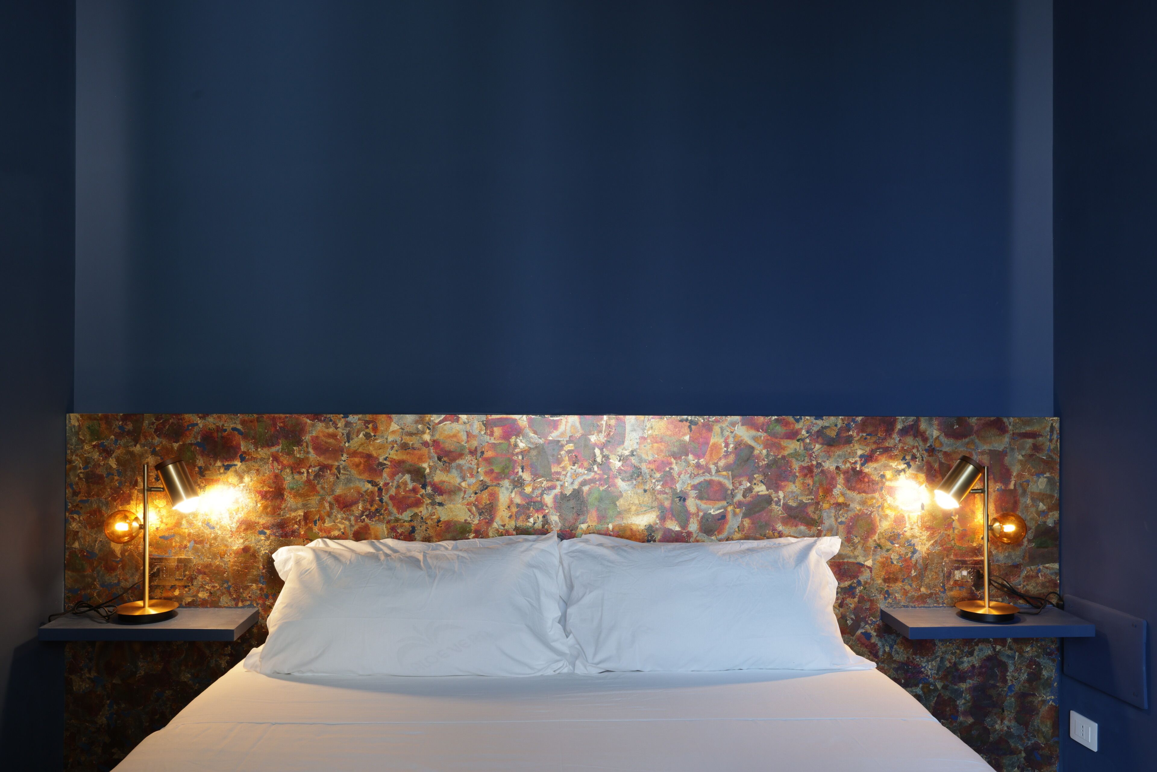 A bed with white linens, two bedside lamps, and a textured wall behind.