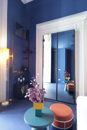 Una habitación con una pared azul, un espejo grande, una mesa redonda con un florero y un reposapiés rojo.