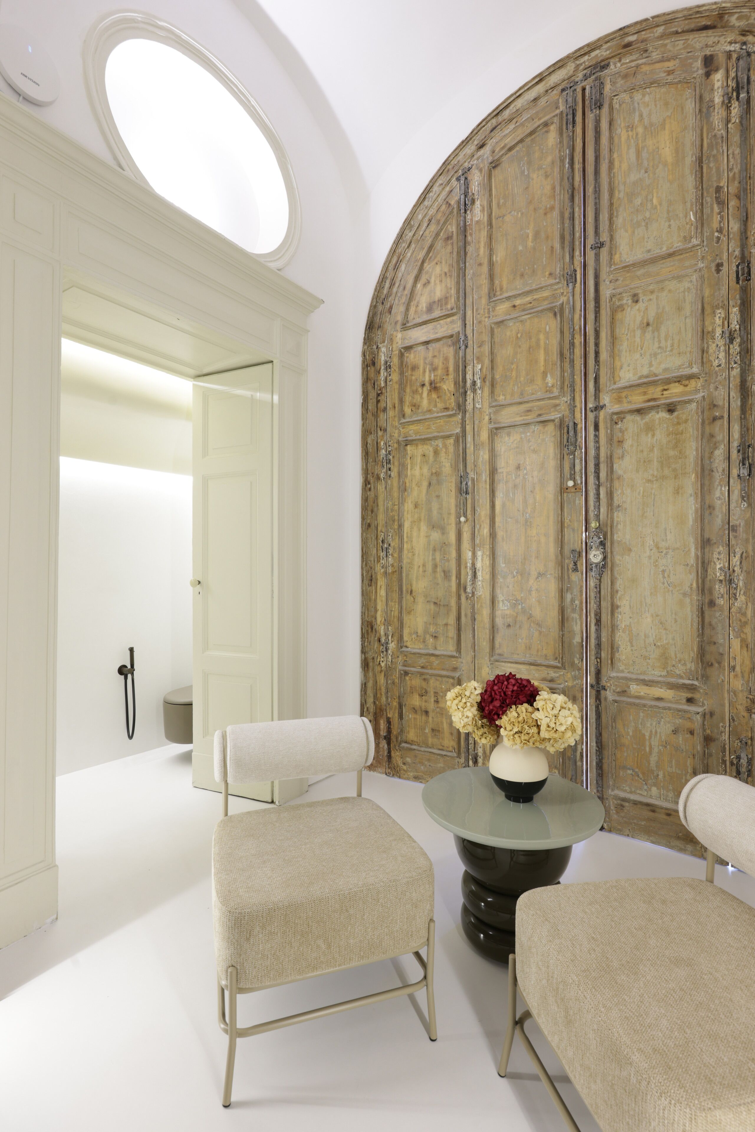 Una habitación con dos sillones tapizados, una mesa redonda con un florero y una puerta grande de madera.