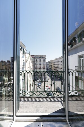 Vista desde un balcón con barandilla de metal, que da a una calle con coches aparcados y edificios.