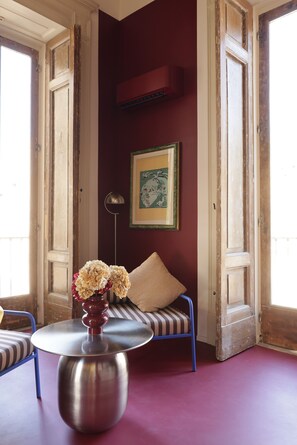A room with a round metal table, a blue chair, a cushioned bench, and a vase with flowers. - Sancta Nolana (Naples)