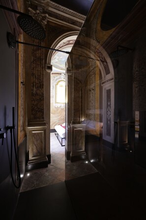 Un pasillo con columnas de mármol, una cama con ropa blanca y vistas a un cuarto con pared decorada.