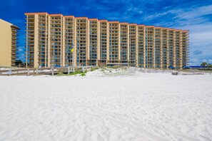 Un hotel moderno de gran altura con varios balcones, ubicado en una playa de arena bajo un cielo despejado.