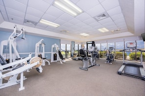 Ett gym med olika typer av träningsutrustning, stora fönster och utsikt över omgivningarna.